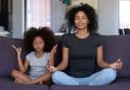 Mulher adulta e menina sentadas em sofá. Elas praticam meditação.