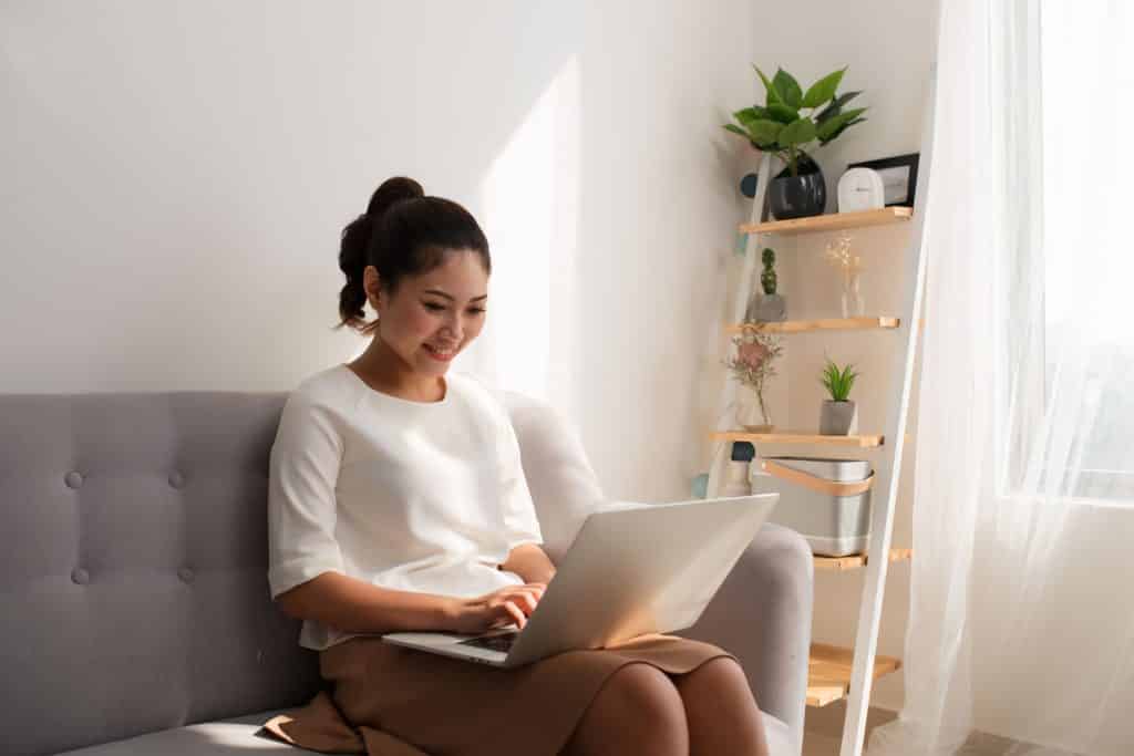 Mulher sentada no sofá mexendo no computador.