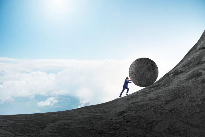 Homem empurrando uma grande pedra para o topo de montanha.