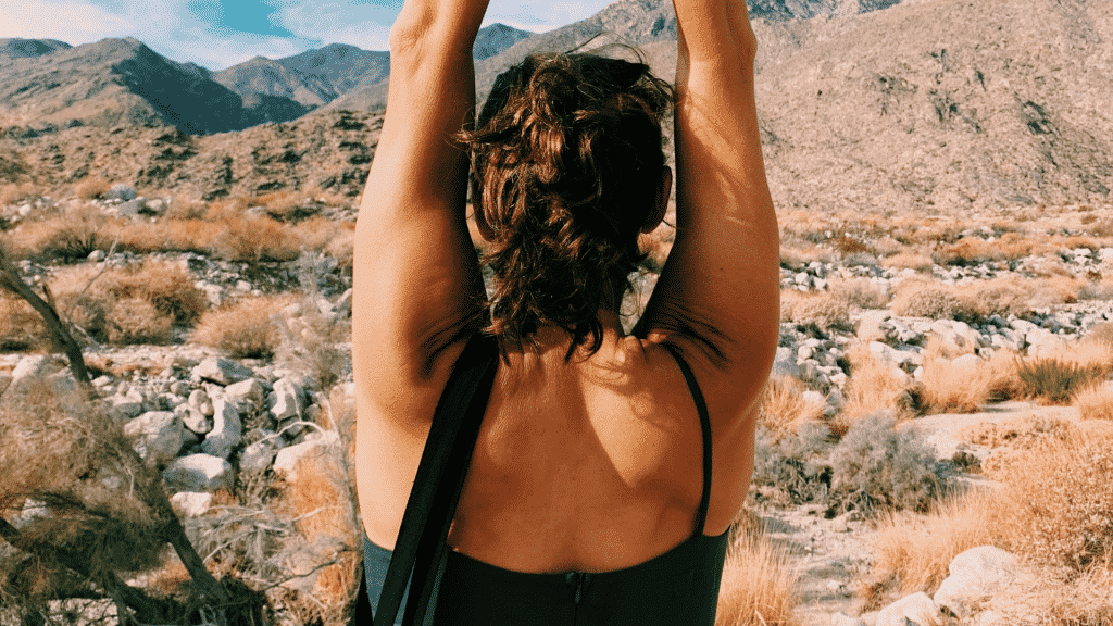 Mulher com os braços erguidos subindo a montanha