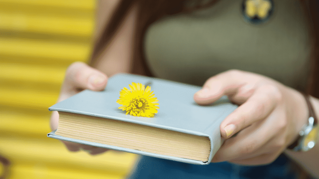 Mulher oferecendo um livro com uma flor em cima