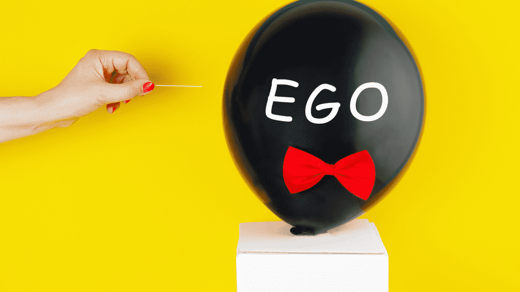 Mulher prestes a estourar um balão preto escrito "ego" com palito de dente