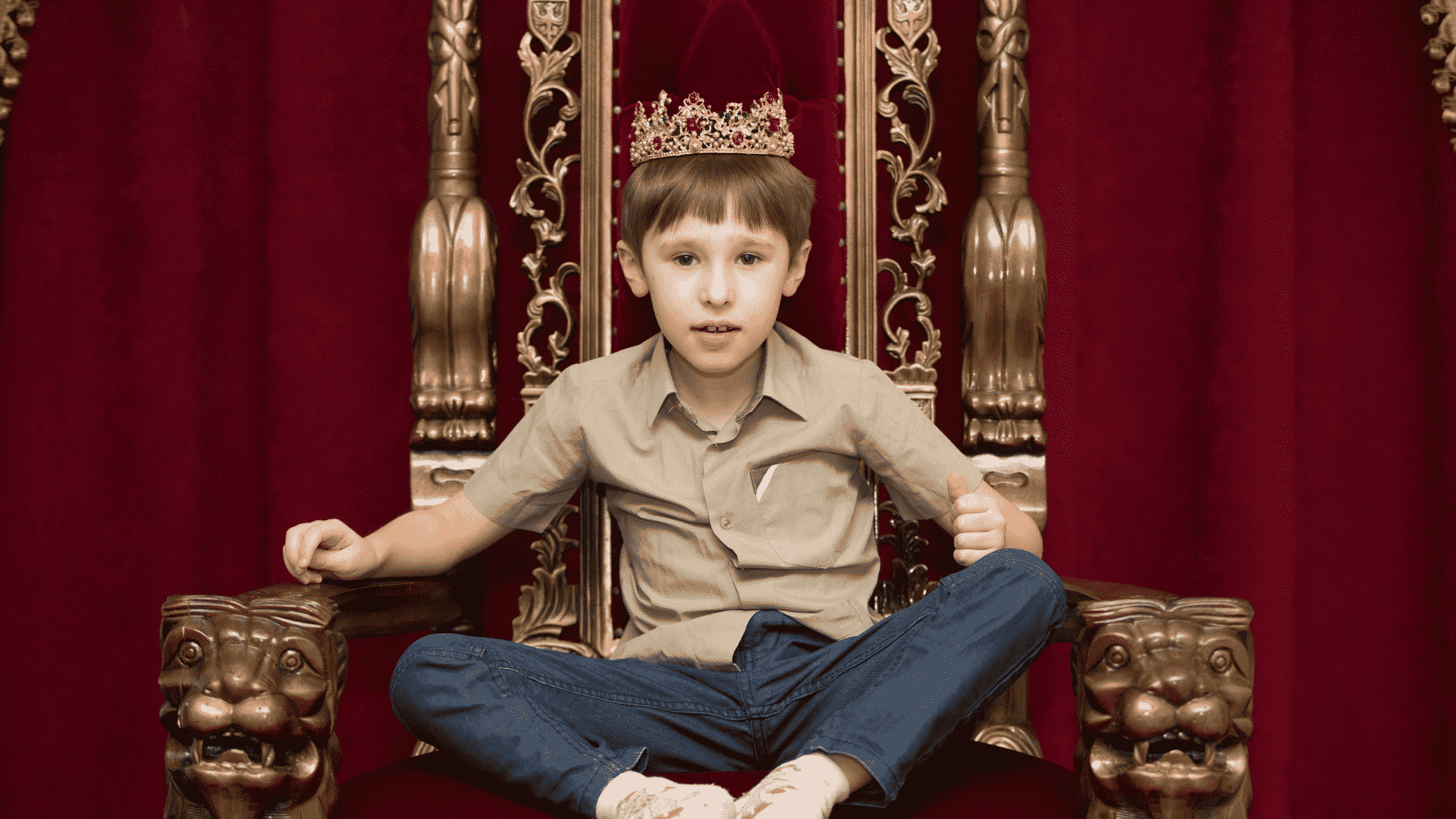 Garoto sentado com as pernas cruzadas em trono usando uma coroa de rei