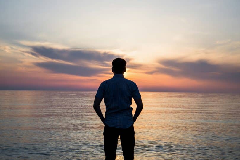 Silhueta de homem olhando para o pôr do sol e o mar.