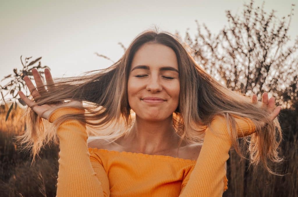 Mulher branca com as mãos no cabelo e olhos fechados, com uma expressão calma.