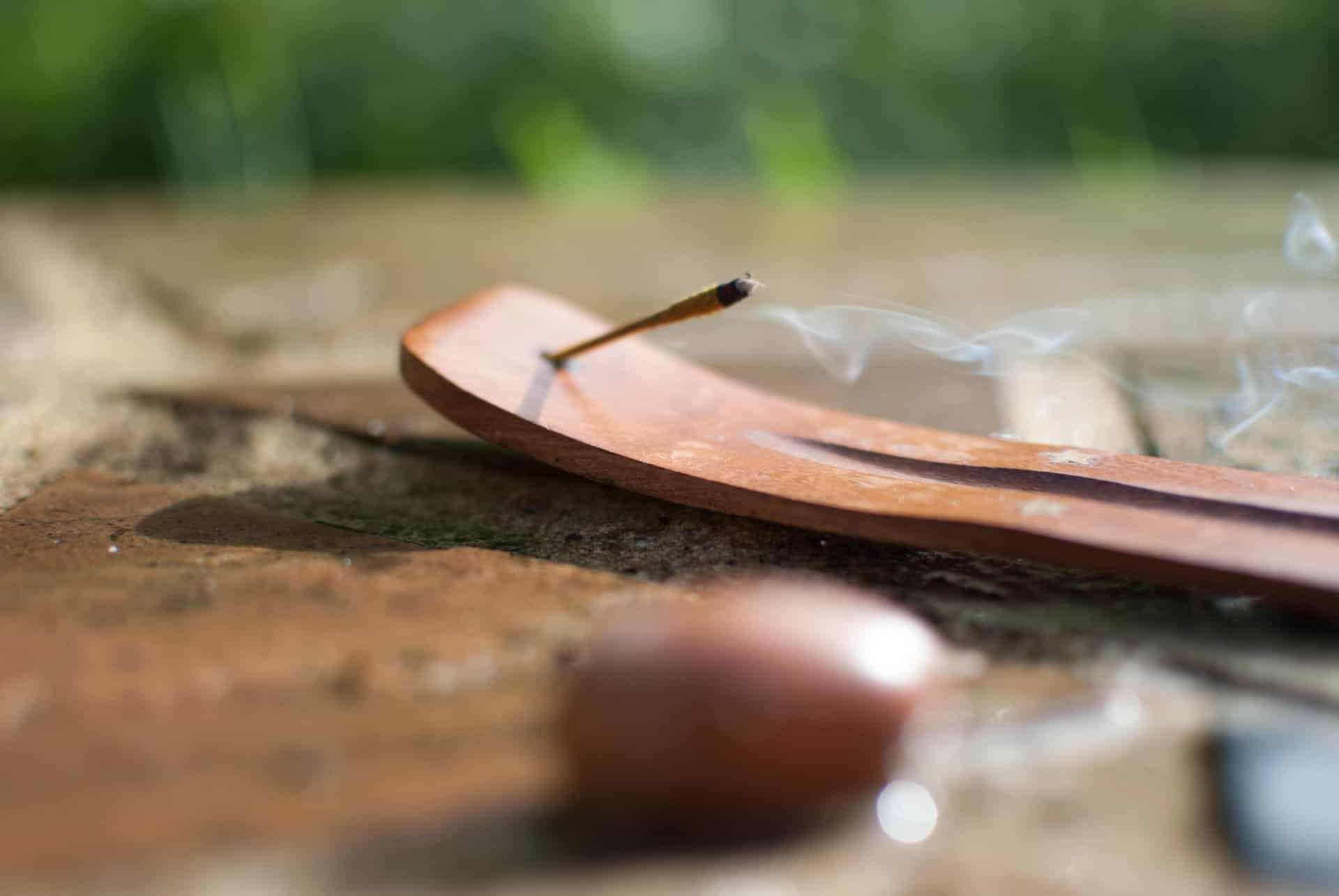Imagem de um incensário sobre uma mesa de madeira. Nele está sendo queimado um incenso de massala. Ao lado dele, uma pedra pequena na cor marrom.

