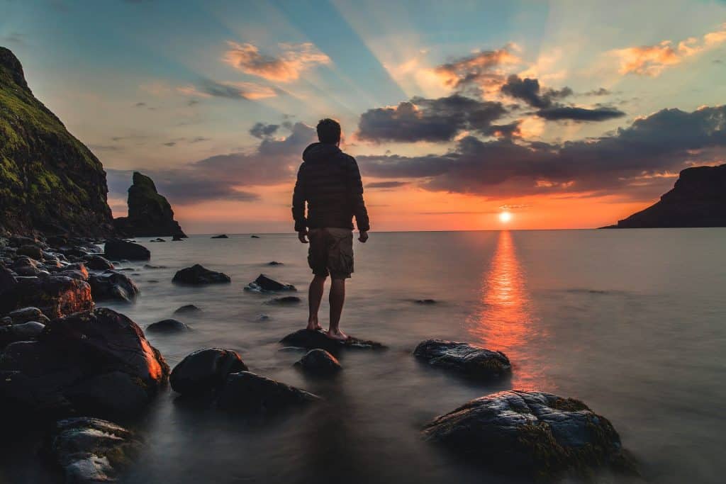 Homem de costas numa praia no pôr-do-sol.