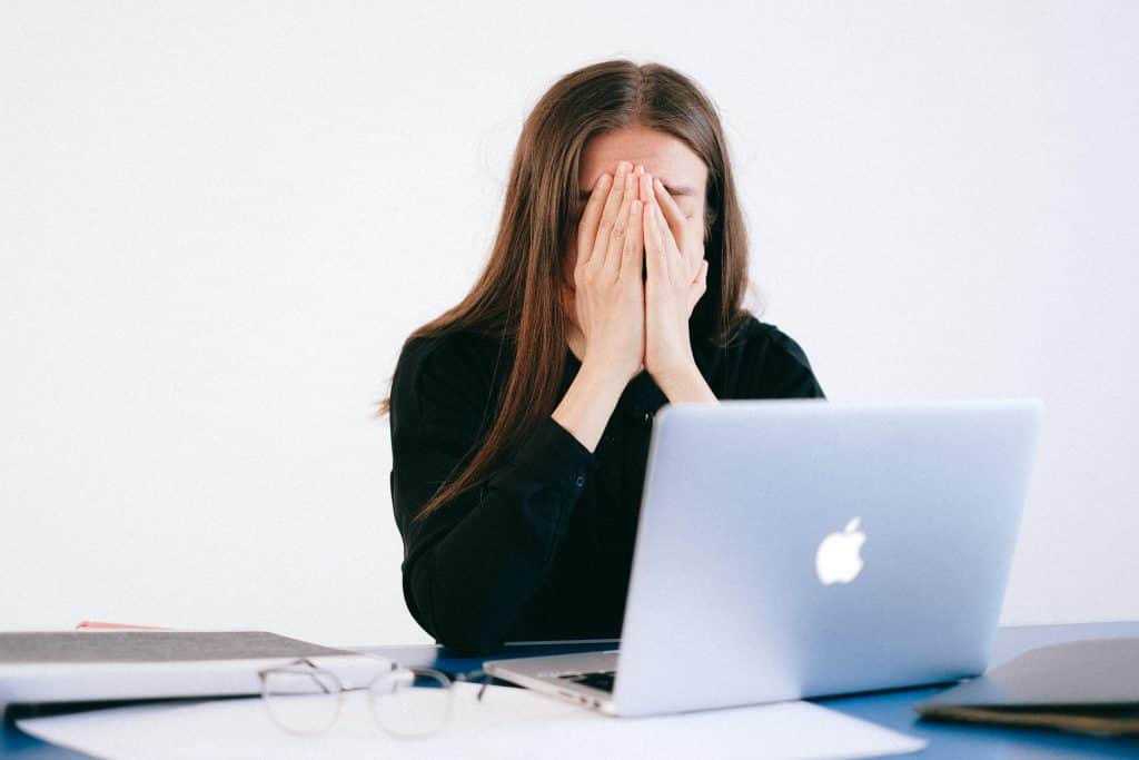 Mulher de frente para o notebook com as mãos em seu rosto