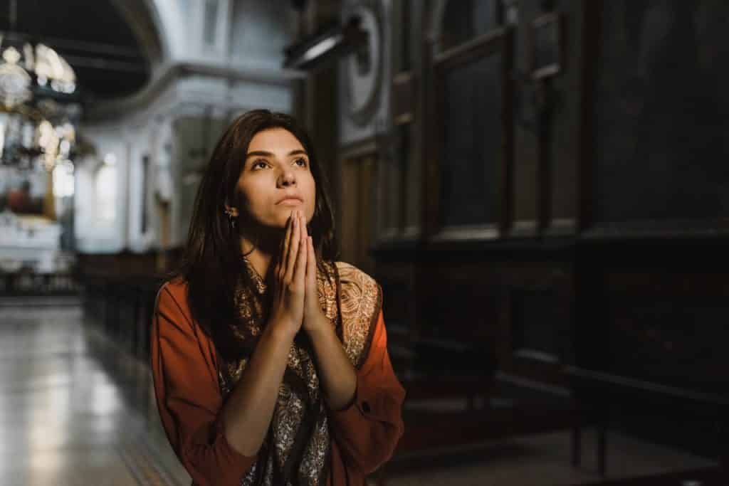 Mulher branca com as mãos juntas na igreja.