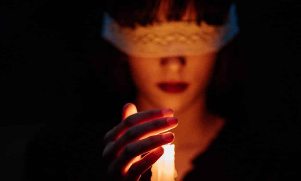 Mulher com os olhos vendados segura vela acesa.