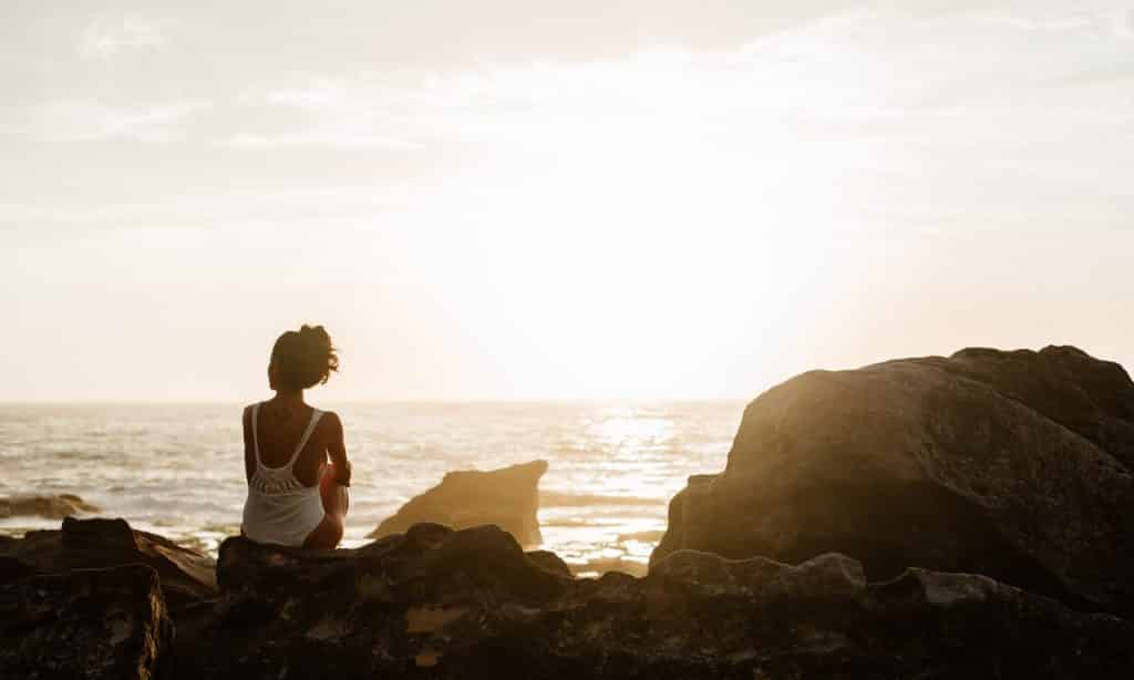 Mulher sentada sobre pedras observa o mar. 