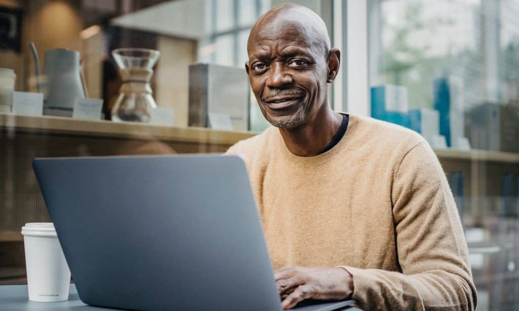 Homem sentado à mesa mexe em computador.