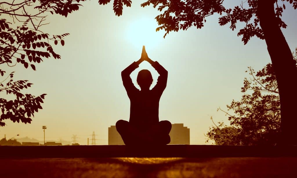 Um pessoa sentada no chão de uma praça meditando em frente ao Sol.