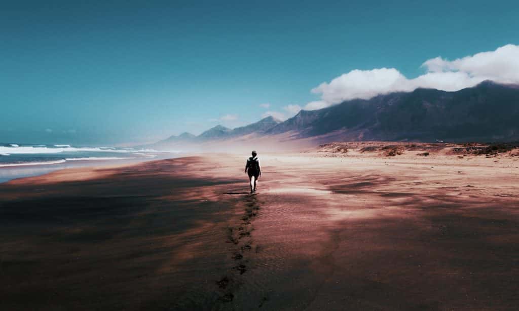 Homem anda na areia em direção às montanhas. 