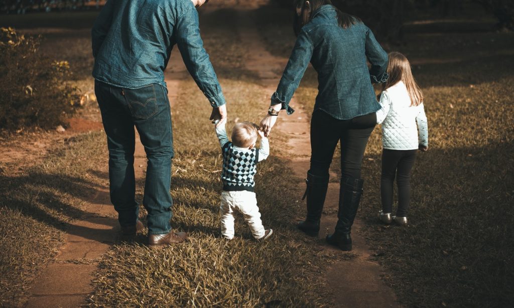 Família composta por duas crianças e dois adultos caminha em ambiente externo.