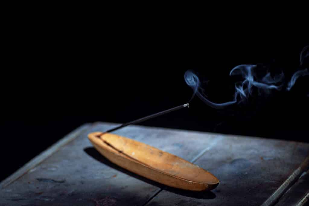 Imagem de fundo preto e em destaque um incensário de madeira e dentro dele um incenso de sálvia sendo queimado. O incensário está sobre uma mesa de madeira.