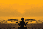Pessoa meditando na praia durante o pôr do sol