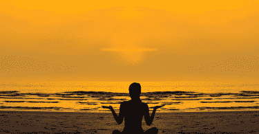 Pessoa meditando na praia durante o pôr do sol