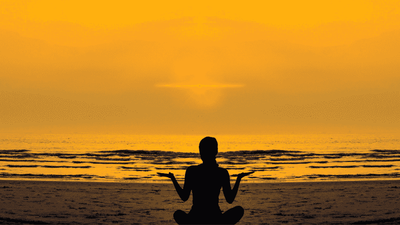 Pessoa meditando na praia durante o pôr do sol