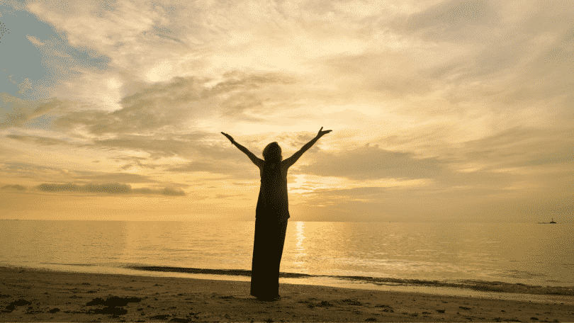Silhueta de mulher com os braços erguidos na praia