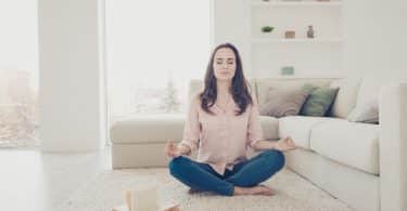 Mulher branca meditando no chão de uma sala.