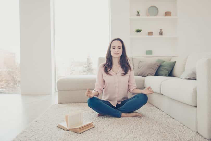 Mulher branca meditando no chão de uma sala.