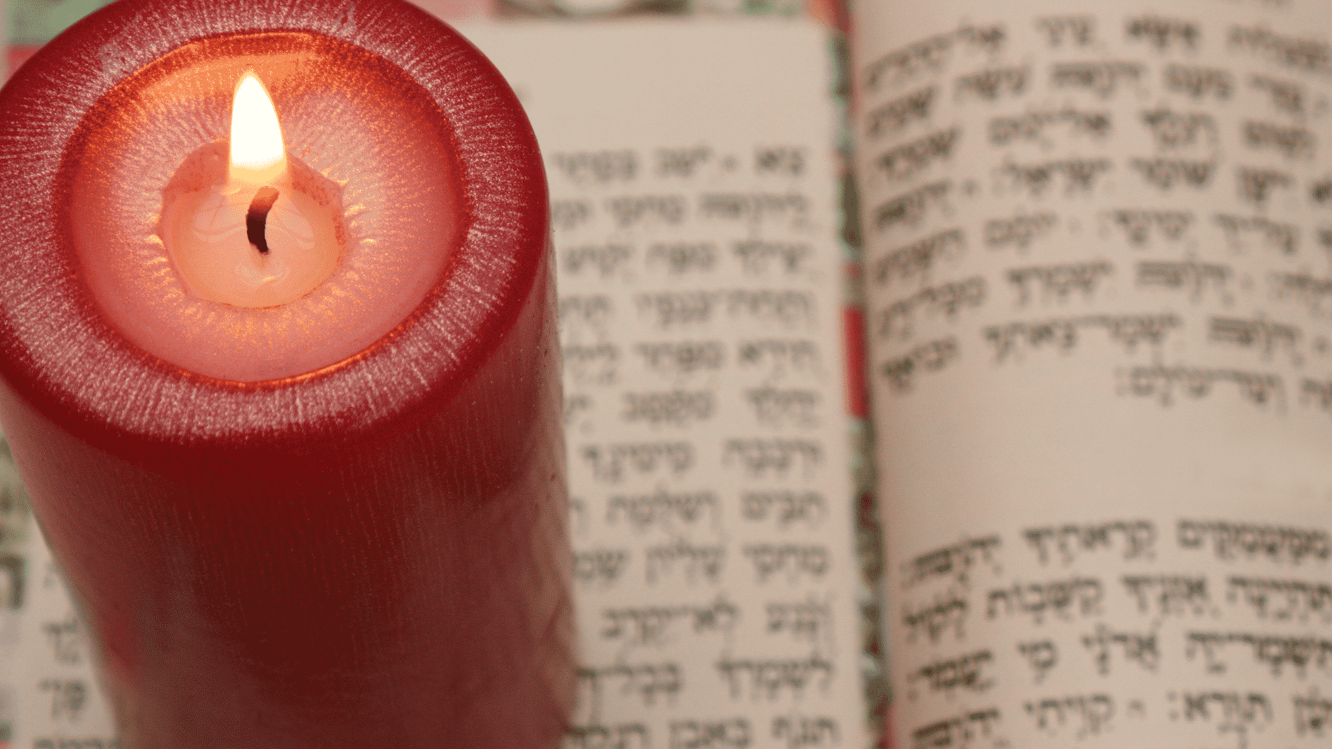 Livro sagrado judaico aberto para estudo da cabala com vela vermelha acesa ao lado