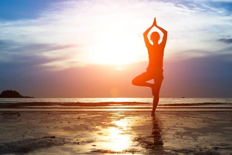 Mulher praticando yoga na praia.