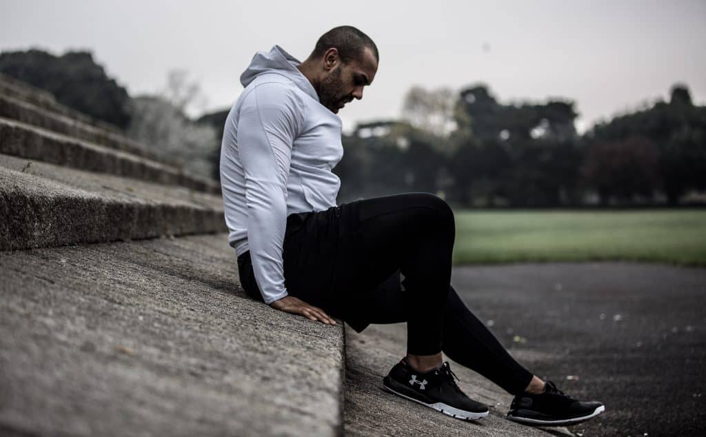 Homem branco usando roupas de ginástica, sentado no concreto.