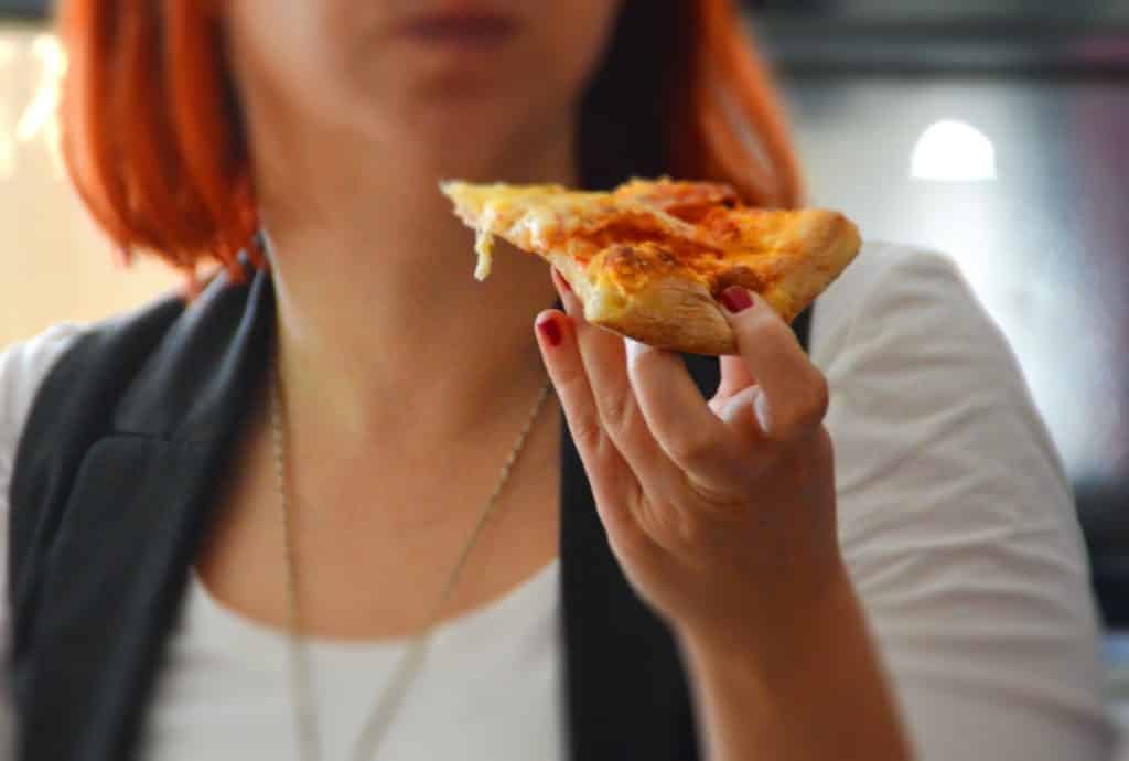 Mulher branca comendo pizza.