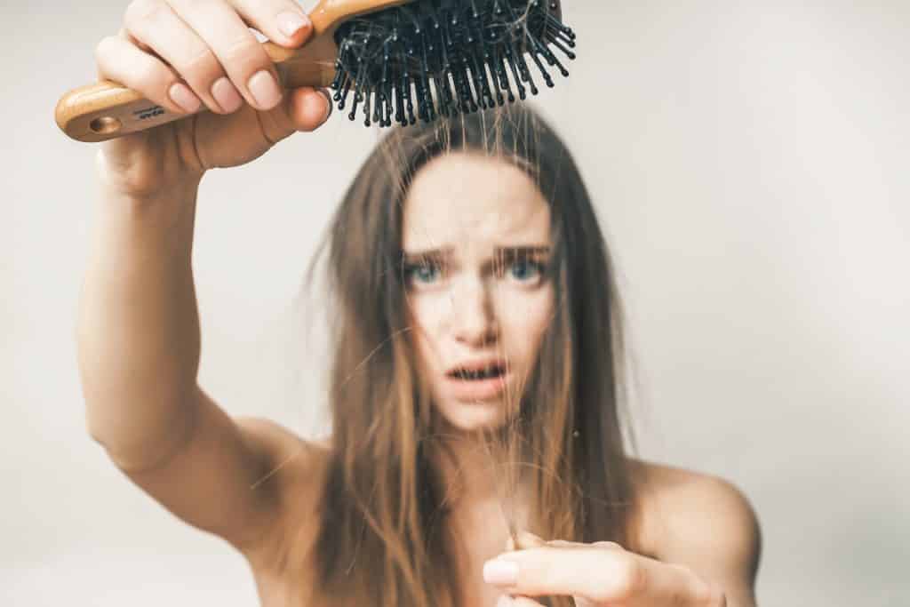 Imagem de uma mulher de cabelos longos. Ela penteou o cabelo e viu que na escova utilizada tinha vários fios que caíram ao pentear.