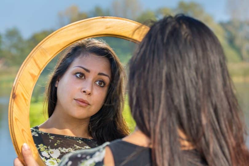 Mulher em ambiente externo se olha em espelho.