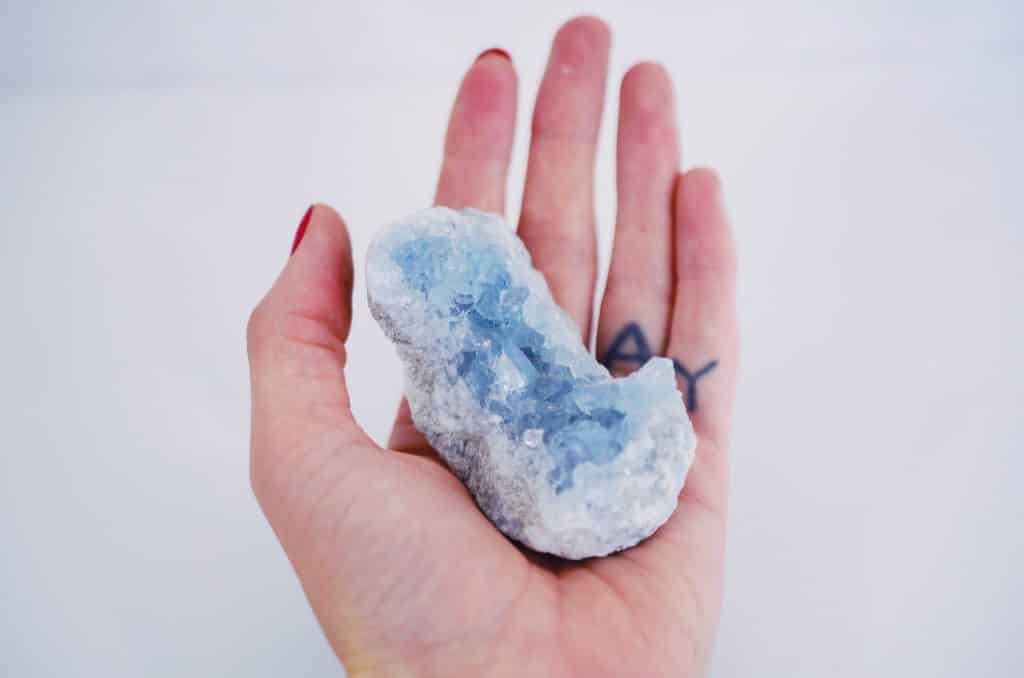 Mão branca feminina segurando cristal azul.