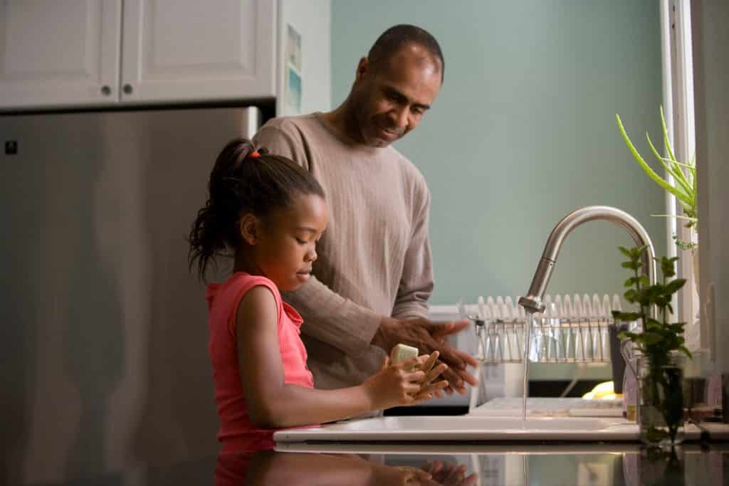 Homem e menina negros lavando as mãos.