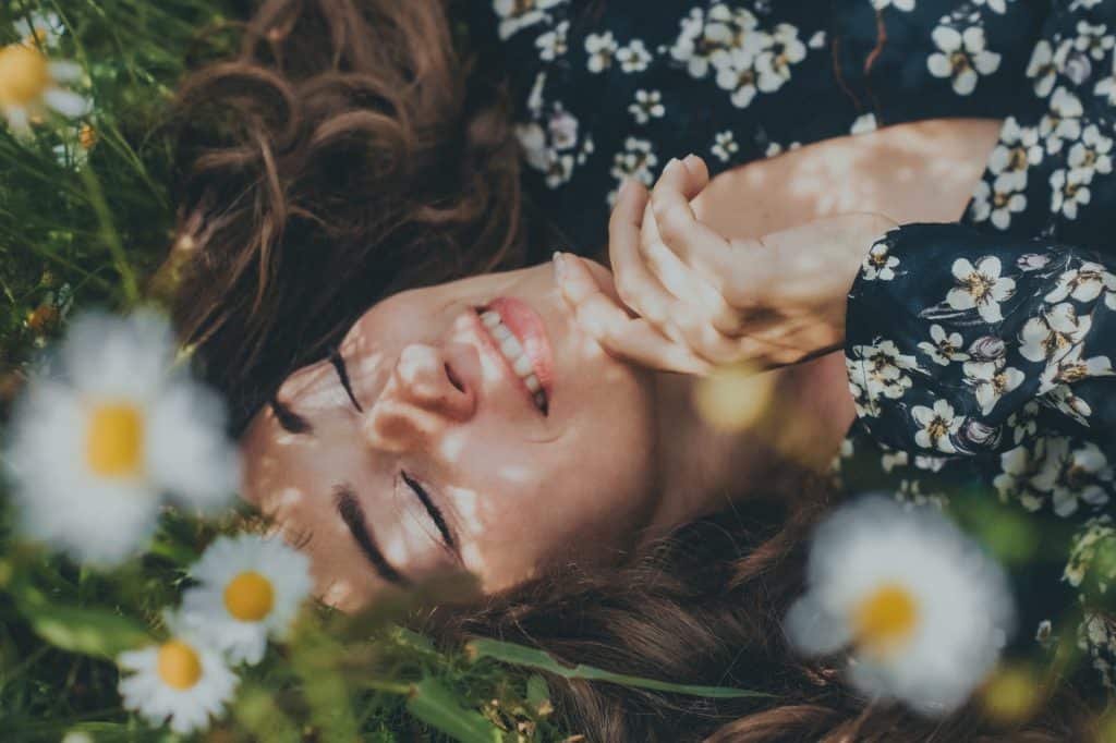 Mulher branca deitada na grama com flores brancas.