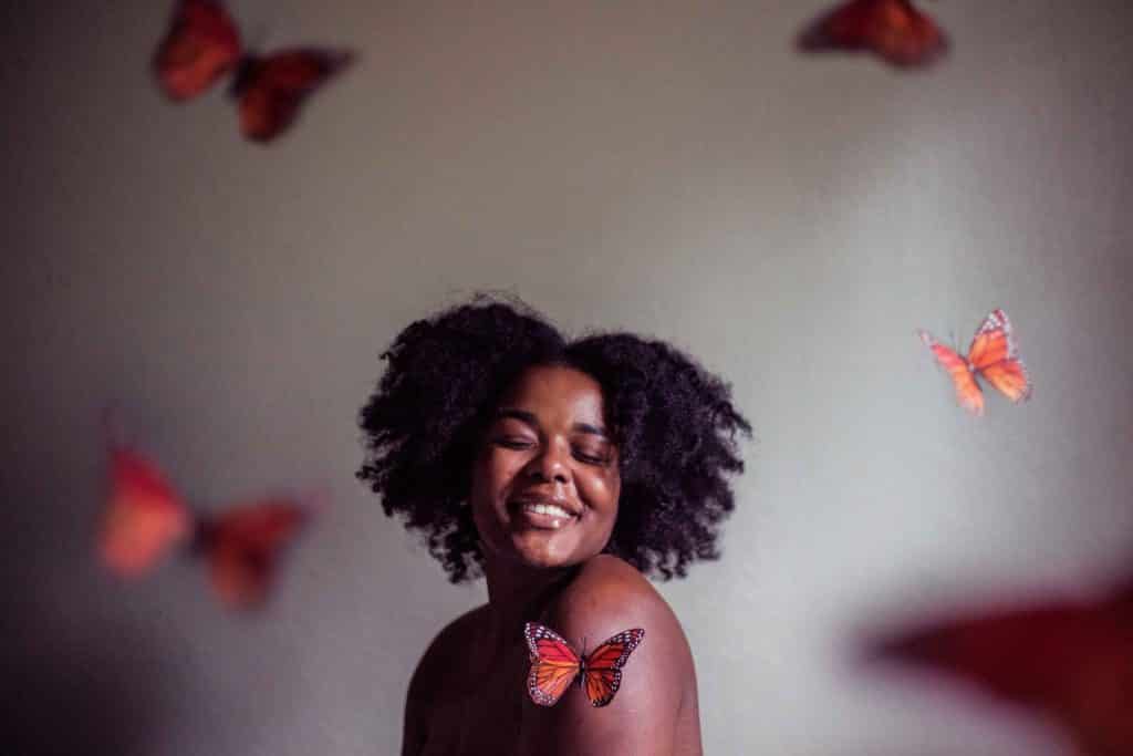 Mulher negra com expressão sorridente rodeada de borboletas.