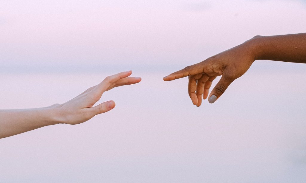 Duas mãos aproximam-se para se tocarem sobre cenário de tonalidade clara. 