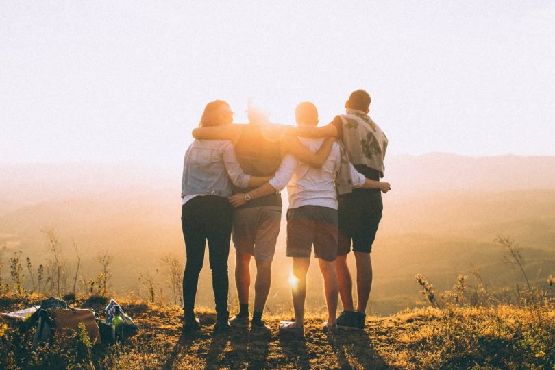 Quatro amigos se abraçando vendo o pôr do sol