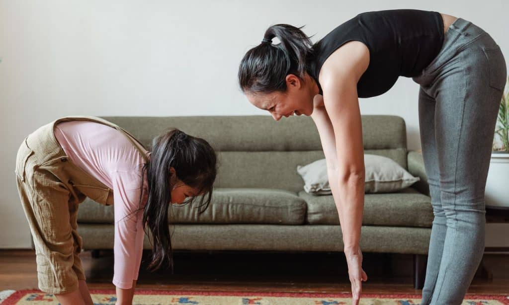 Mulher e menina riem enquanto praticam yoga em sala de estar.