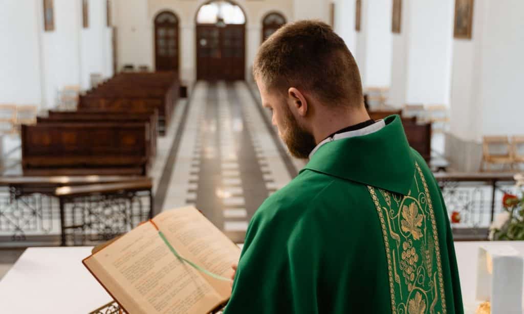 Reverendo lê bíblia em igreja vazia.