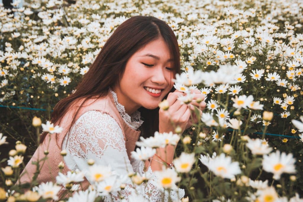 Mulher em um campo de flores sorrindo de olhos fechados