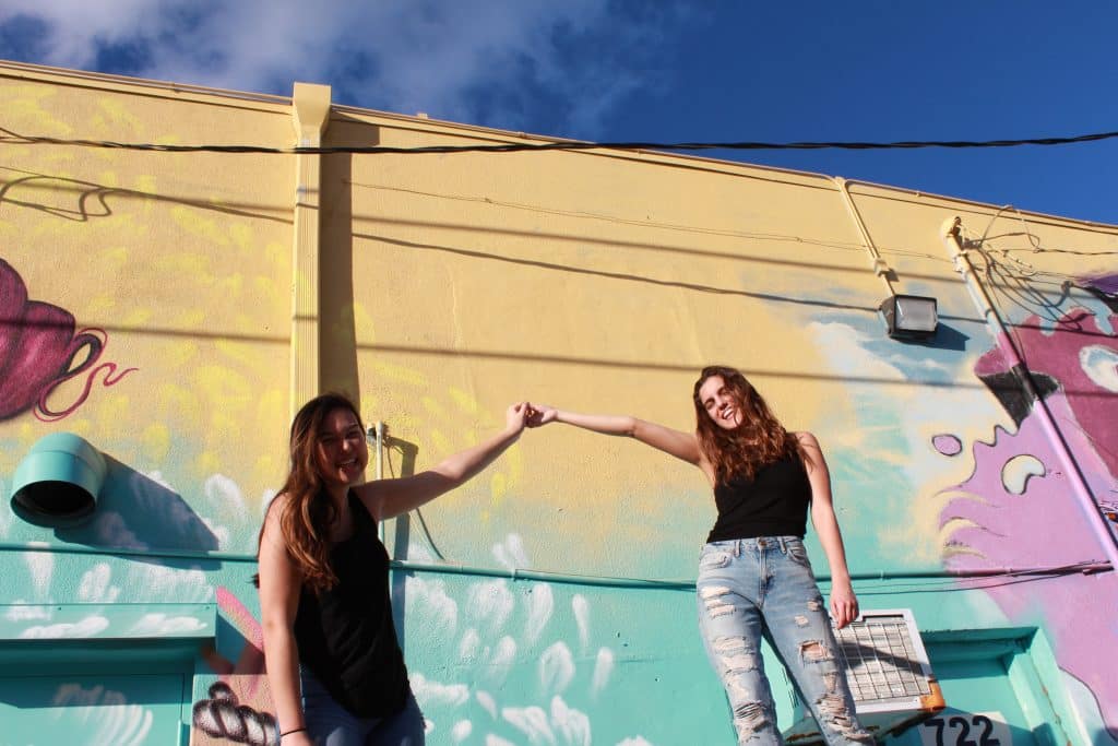 Duas mulheres de mãos dadas e sorrindo na rua