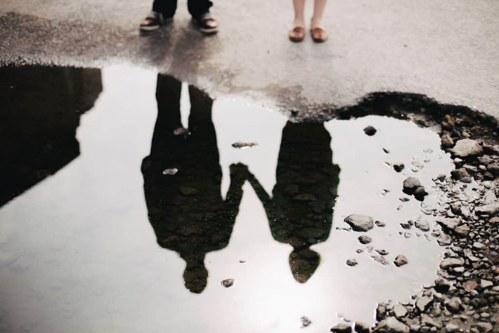 Silhueta de pessoas de mãos dadas refletindo numa poça de água.