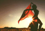 Silhueta de mulher dançando no deserto com lenço vermelho durante por do sol