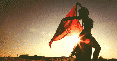 Silhueta de mulher dançando no deserto com lenço vermelho durante por do sol