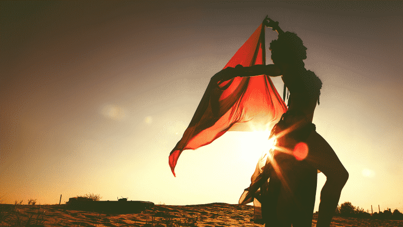 Silhueta de mulher dançando no deserto com lenço vermelho durante por do sol