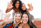 Mulheres amigas tirando selfie sorrindo fazendo sinal de "pare" com a destra