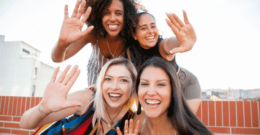 Mulheres amigas tirando selfie sorrindo fazendo sinal de "pare" com a destra