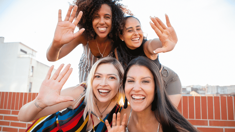 Mulheres amigas tirando selfie sorrindo fazendo sinal de "pare" com a destra