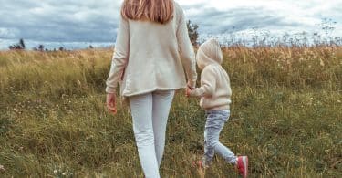 Mulher e criança de mãos dadas andam em campo.